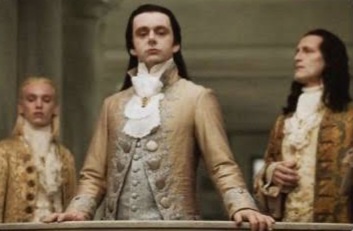 Three men in ornate 18th-century aristocratic attire stand in a grand hall, looking bored or unimpressed. The central…