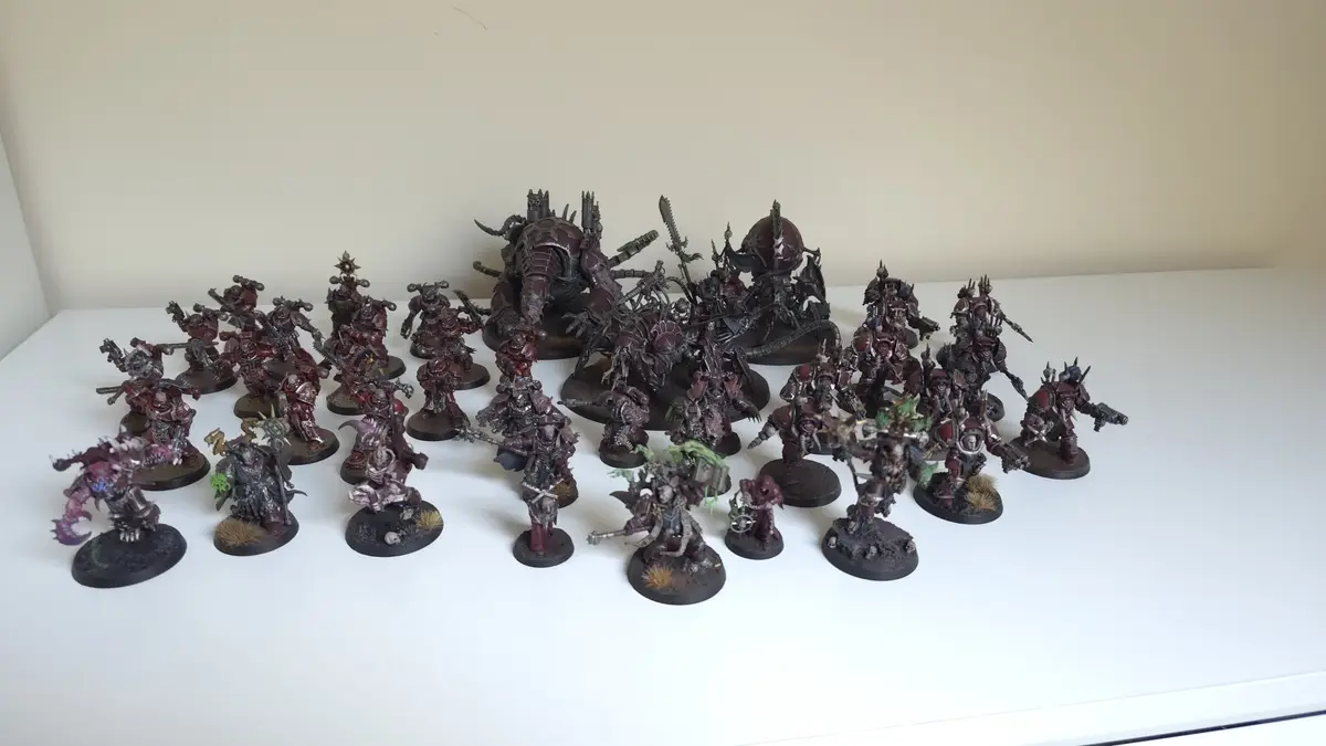 A large collection of painted miniature figurines, mostly dark red and black, depicting fantasy warlike creatures and…