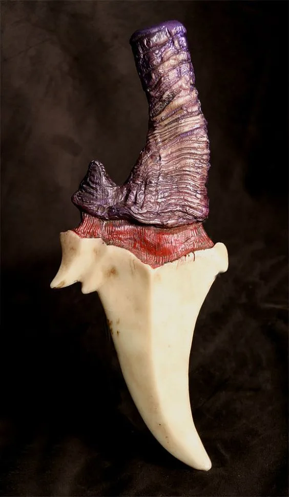 a real shark tooth is mounted on a dark background and has been artistically modified to resemble a boot, with a purple…