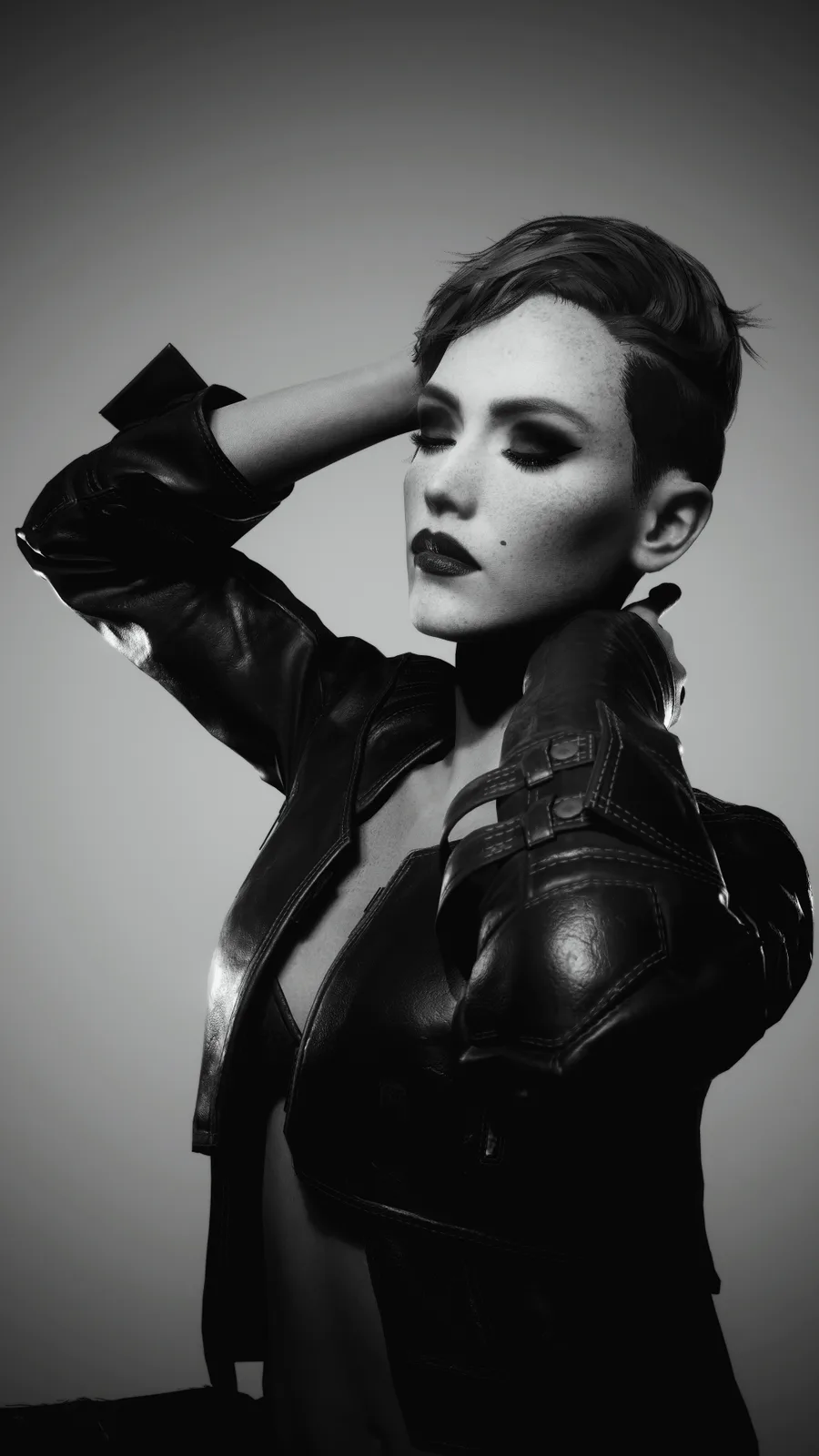 A black-and-white photo of a woman with short hair wearing a leather jacket, one hand behind her head and the other pointing…