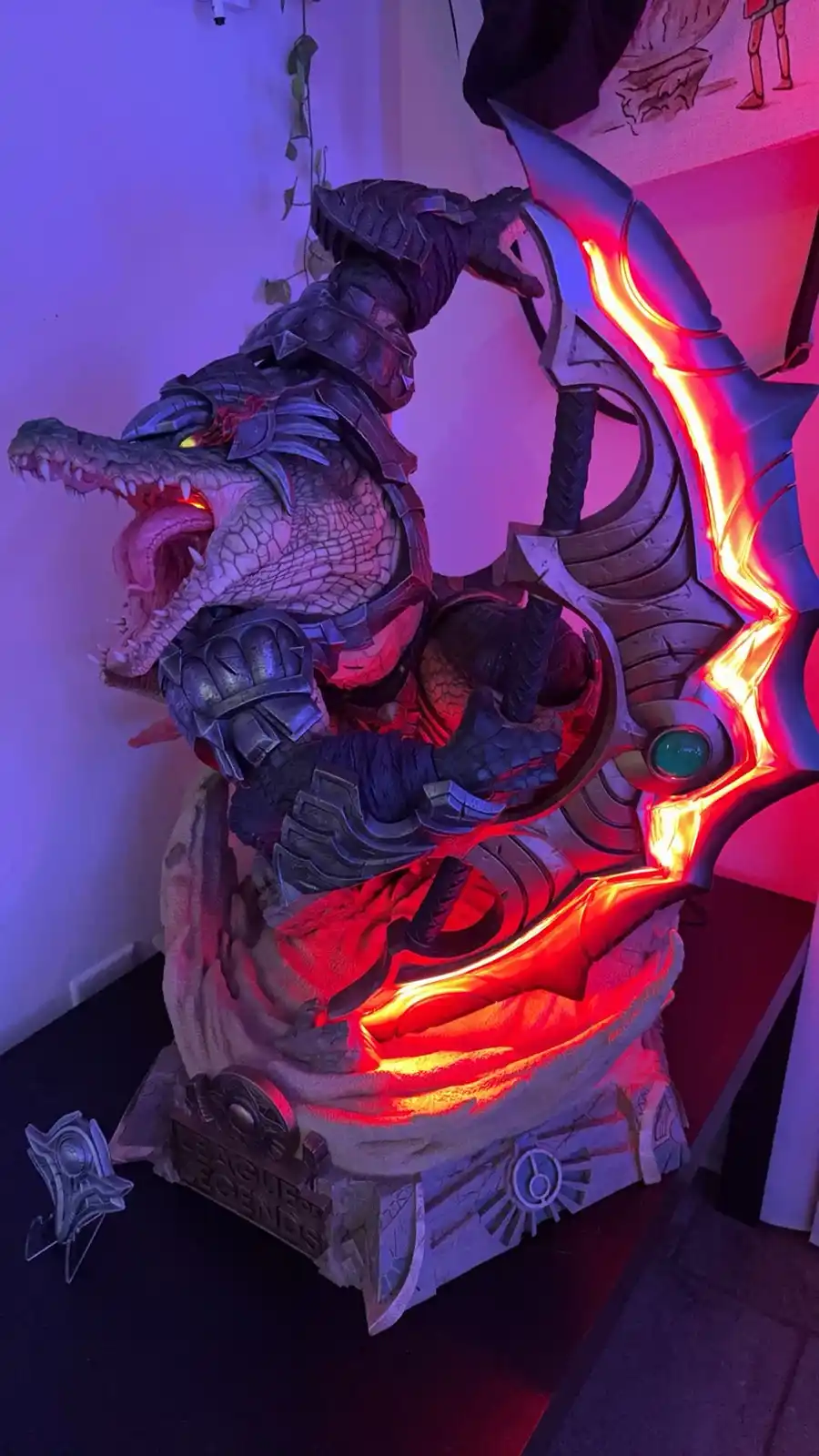A detailed, illuminated statue of the League of Legends character Draven, depicted as a crocodile-like creature in armor…