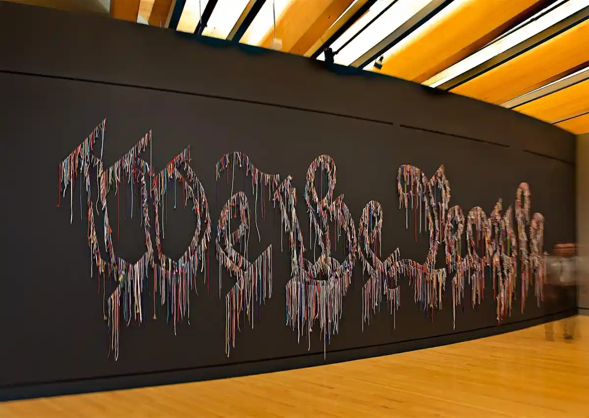 A large-scale art installation on a dark wall spells out 'today is a good day' using colorful, fringed ribbons that appear…