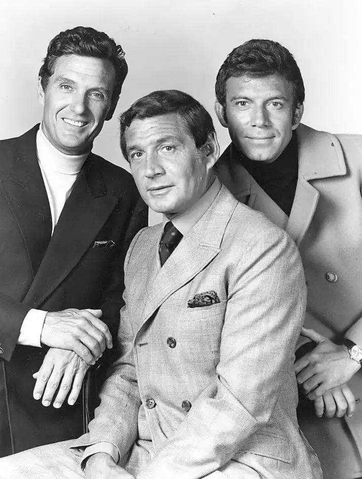 A black-and-white promotional photo of three men from the 1960s, likely the cast of 'The Mod Squad,' posed together. The man…