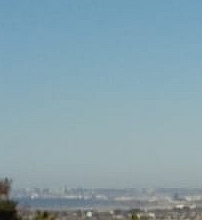 A blurry, distant view of a city skyline under a clear blue sky, with faint buildings and haze visible on the horizon…