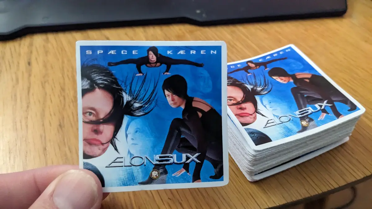 A hand holds up a single card from a stack of identical cards, both showing the same image of a woman in a black outfit with…