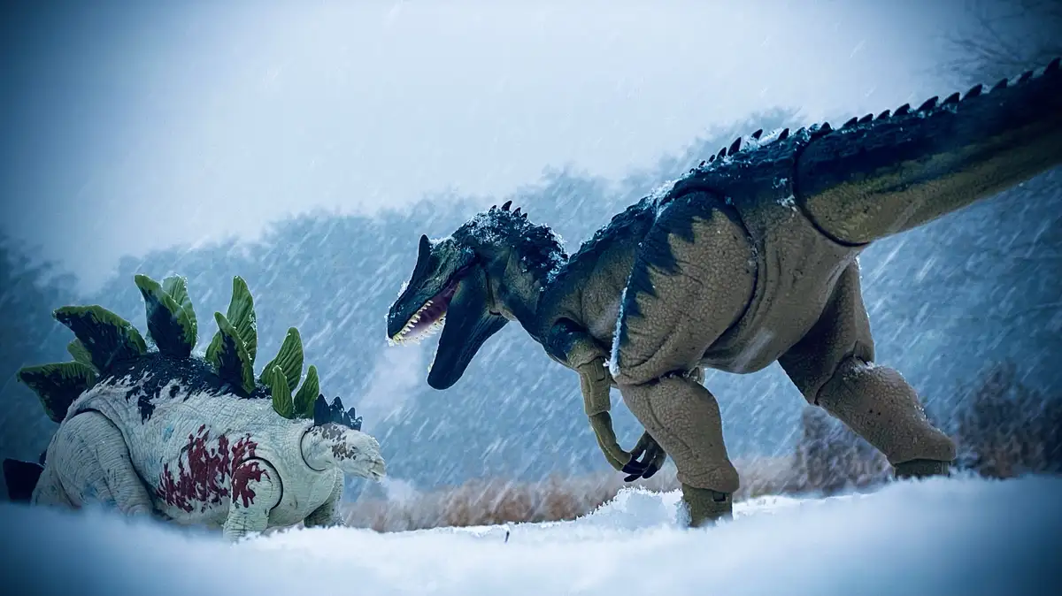 Two toy dinosaurs, a Stegosaurus with red paint resembling blood and a larger predator, are in a snowy landscape. The…