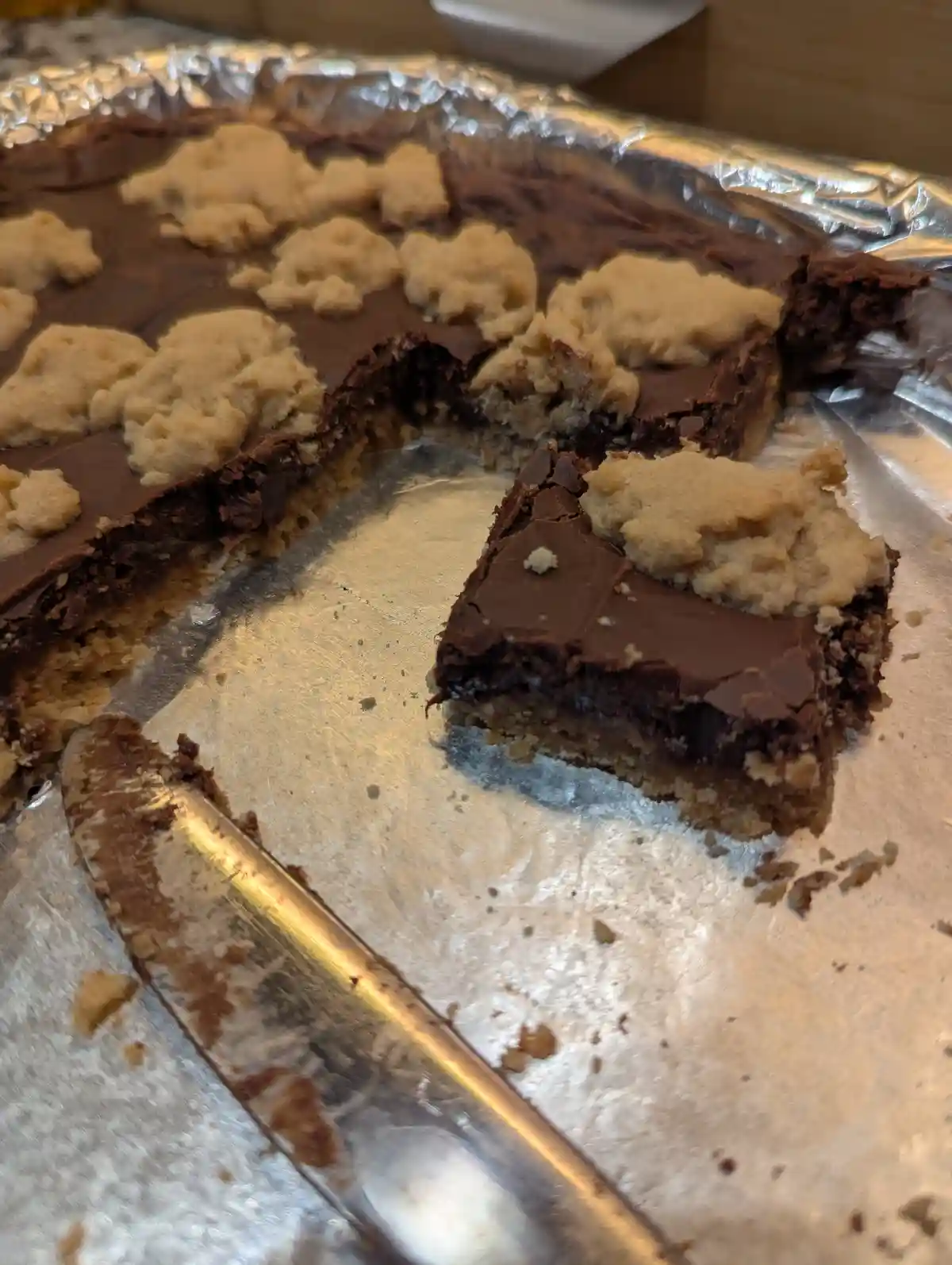 A close-up photo shows a partially eaten chocolate cake with a crumbly, light-brown cookie-like topping, sitting on aluminum…