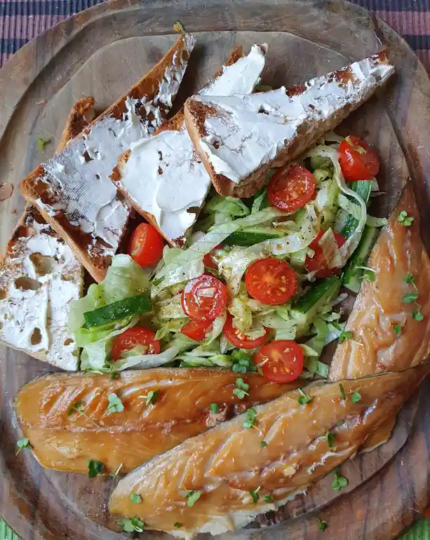 An overhead shot of a wooden platter holding three salmon fillets, a side salad with lettuce, cucumber, and halved cherry…