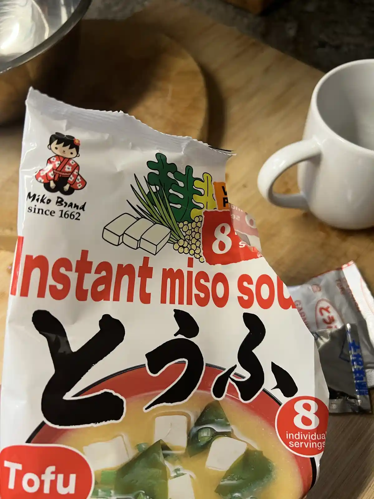 A close-up photo shows a white package of 'Miko Brand' instant miso soup with tofu, featuring a cartoon girl, illustrations…