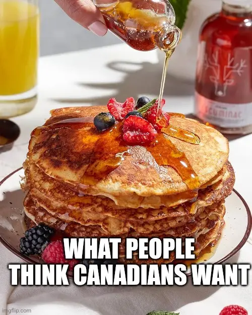 A tall stack of golden-brown pancakes topped with fresh berries and syrup being poured over them from a bottle. A glass of…