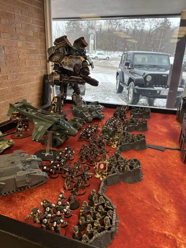 A display of intricately painted Warhammer 40,000 miniatures, including a large black and gold armored walker, tanks, and…