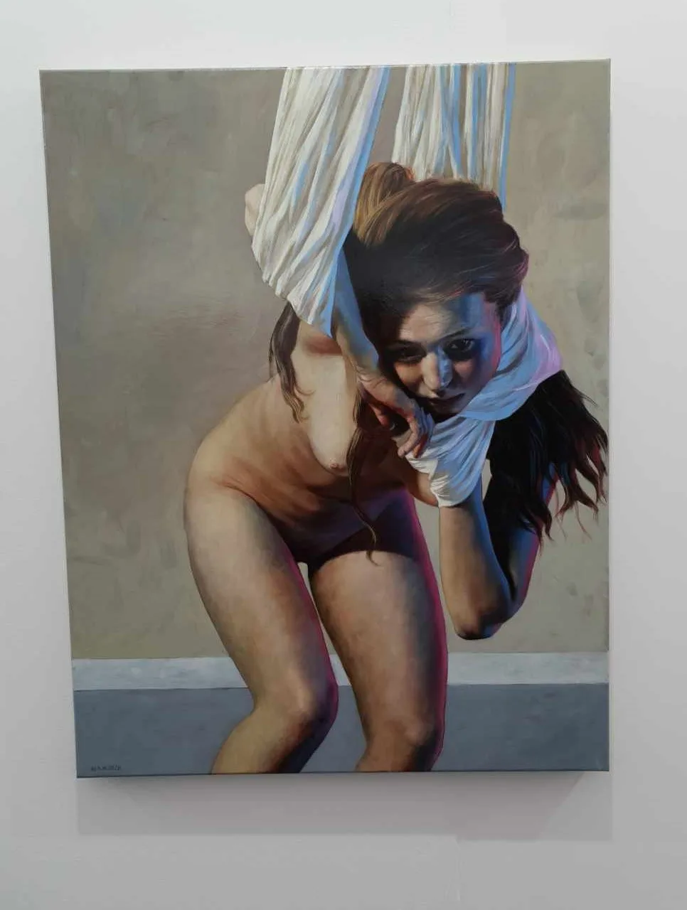 A painting of a nude woman with dark hair, partially draped in white fabric, crouching and looking forward with a serious…