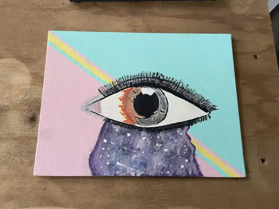A hand-painted canvas depicts a large, stylized eye with black lashes, a galaxy-patterned lower lid, and a fiery orange…