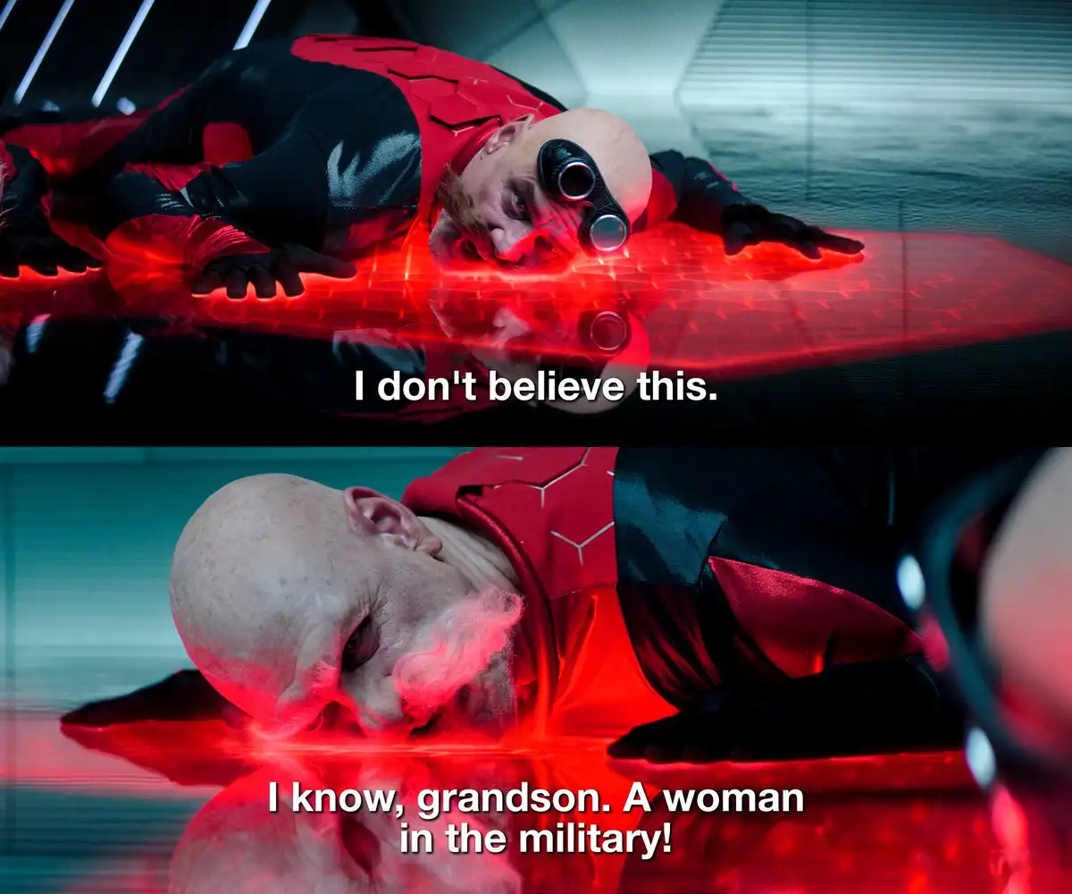 The image shows two panels of a bald man in a red and black suit lying on a glowing red surface. In the top panel, he looks…