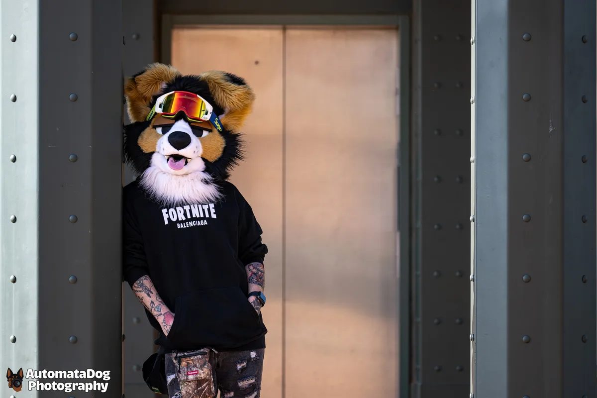 A person in a furry dog costume with a black and tan coat, wearing reflective ski goggles and a black hoodie with 'FORTNITE…