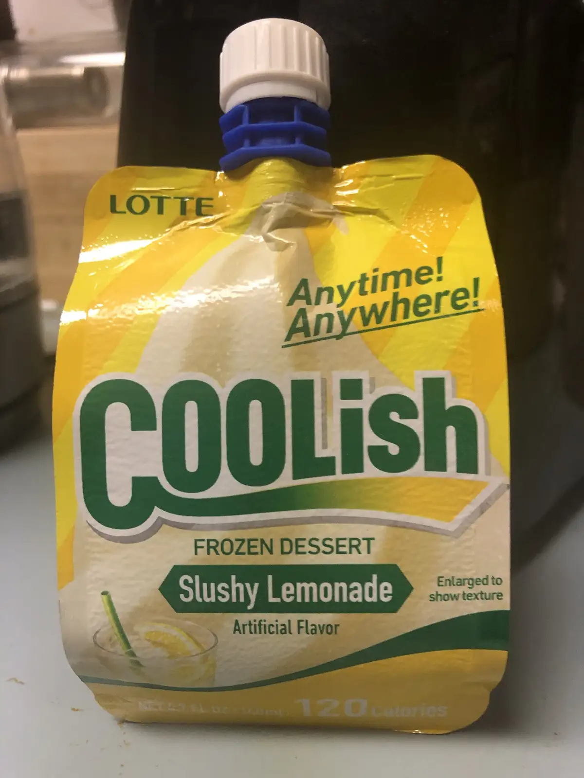 A close-up photo of a yellow and green Lotte Coolish frozen dessert pouch, labeled 'Slushy Lemonade' with 'Artificial…