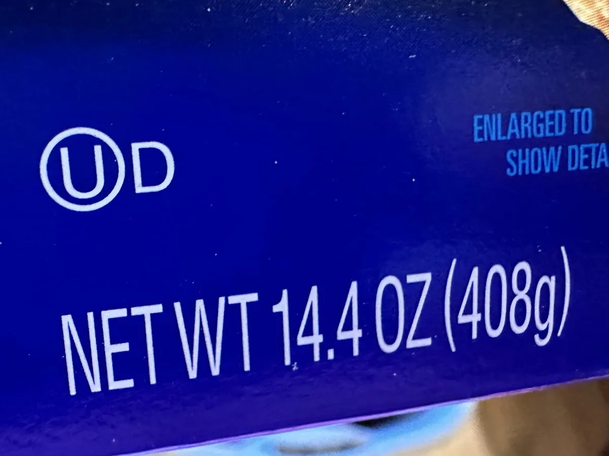 A close-up of a blue product package showing a 'UD' logo, the text 'NET WT 14.4 OZ (408g)', and the partially visible phrase…