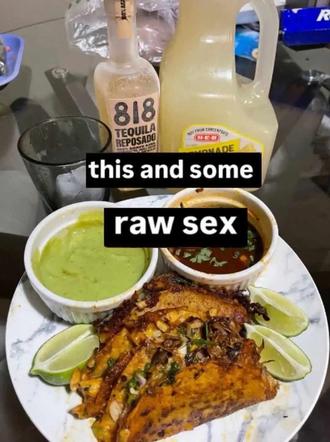 A plate of food, likely tacos or enchiladas, with two small bowls of sauce and lime wedges, sits on a table next to a bottle…