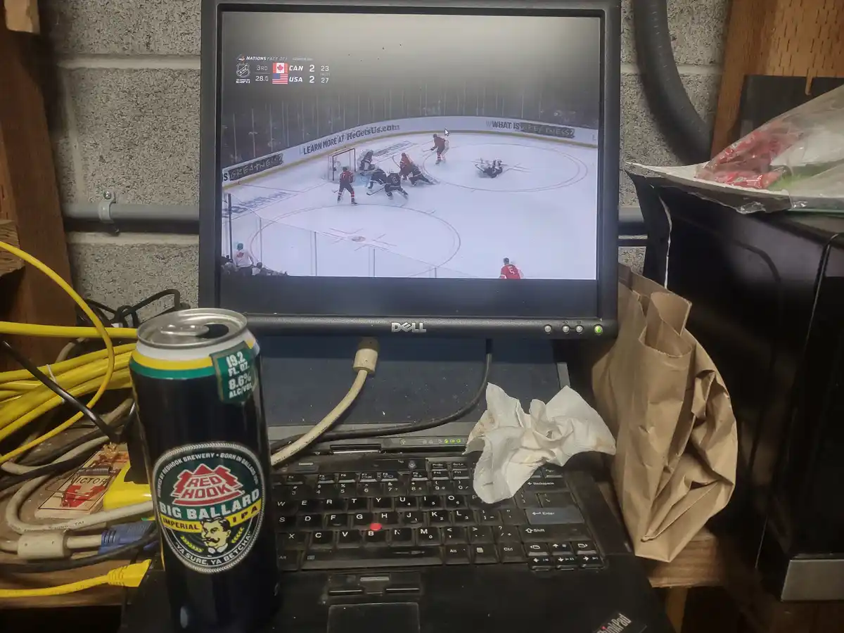 A Dell laptop displays a hockey game between Canada and USA tied 2-2 in the 3rd period, with a player on the ice. A can of…