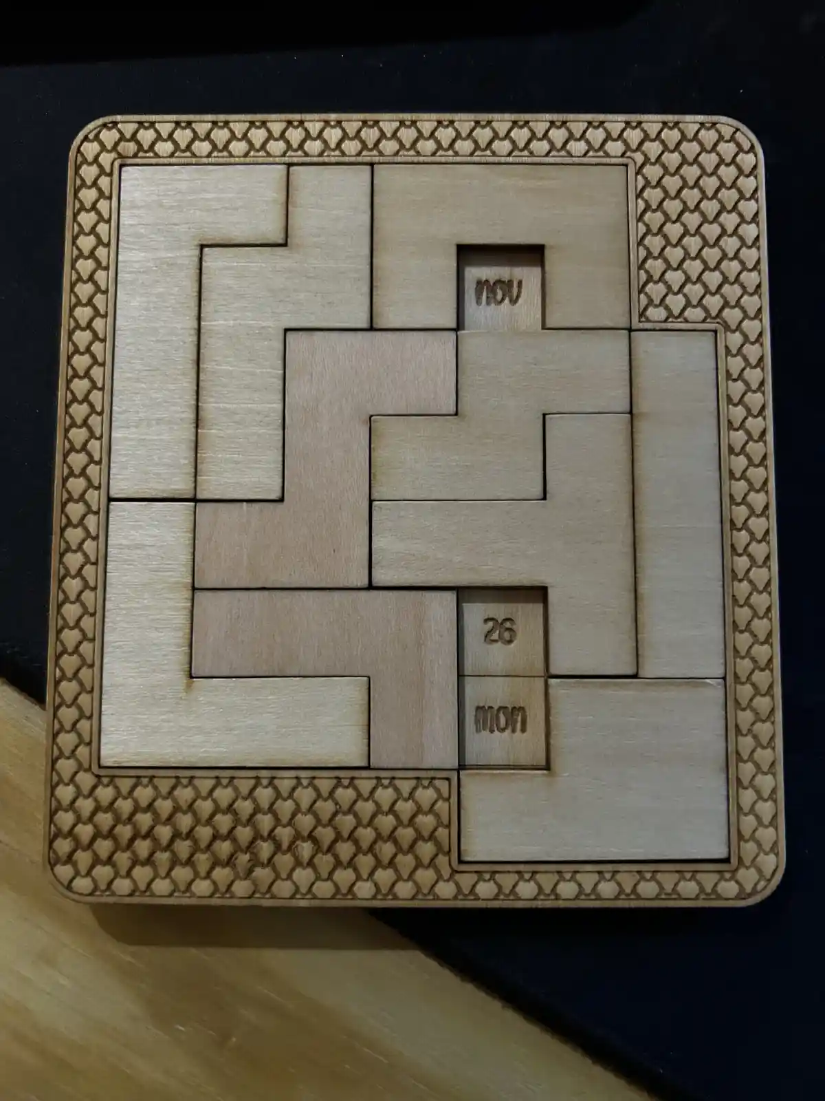 A wooden puzzle calendar with interlocking pieces forming a grid, where two small blocks are visible: one labeled 'nov' and…