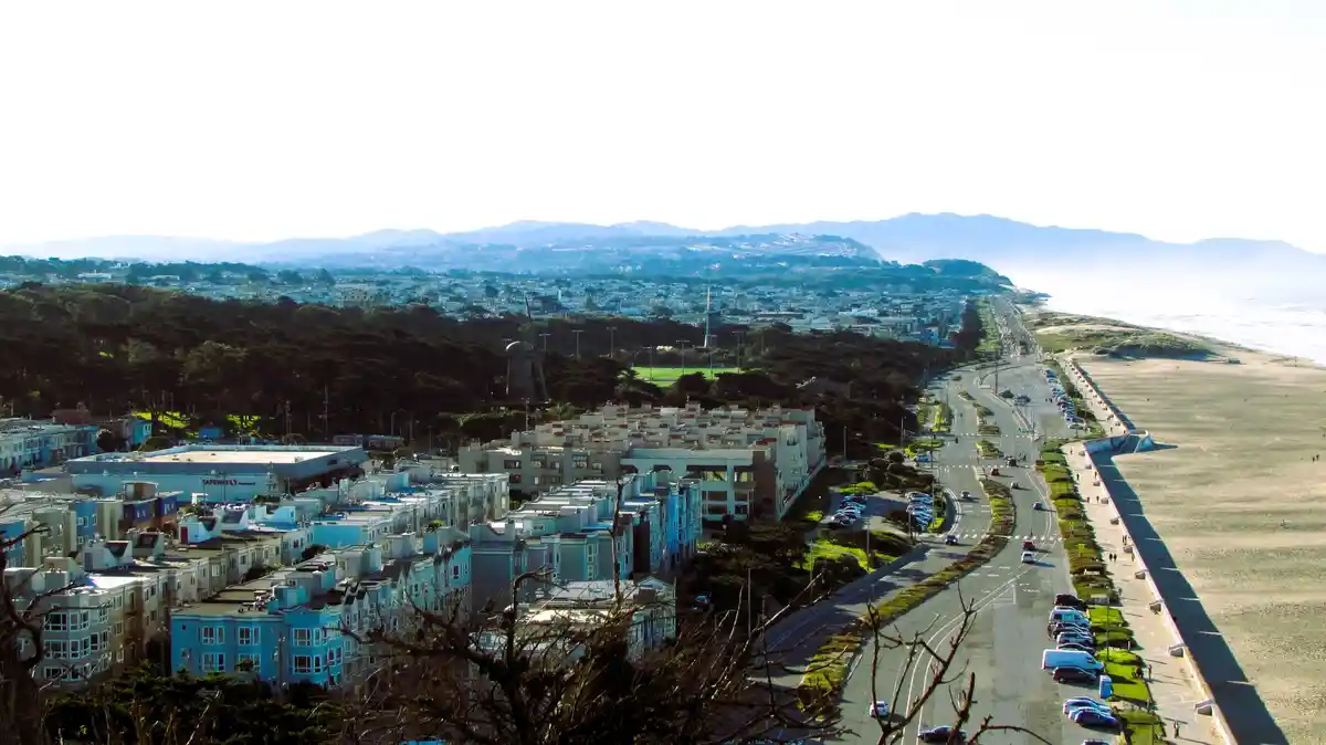 A scenic, high-angle photograph of a coastal cityscape with a winding road alongside a beach, featuring rows of colorful…