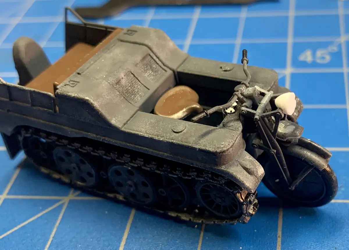 A close-up photo of a detailed scale model of a military half-track vehicle, which has a small motorcycle mounted on its…