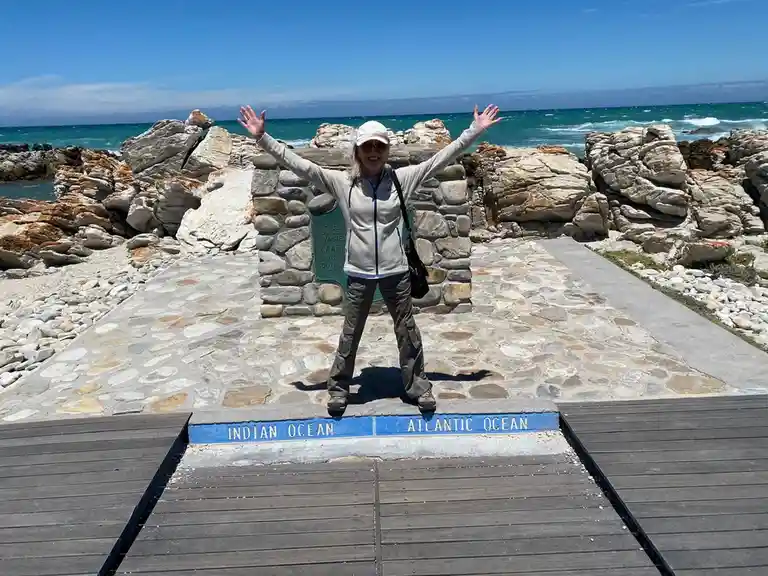 A woman stands with arms outstretched on a wooden boardwalk at a famous geographical landmark where a blue painted stone…