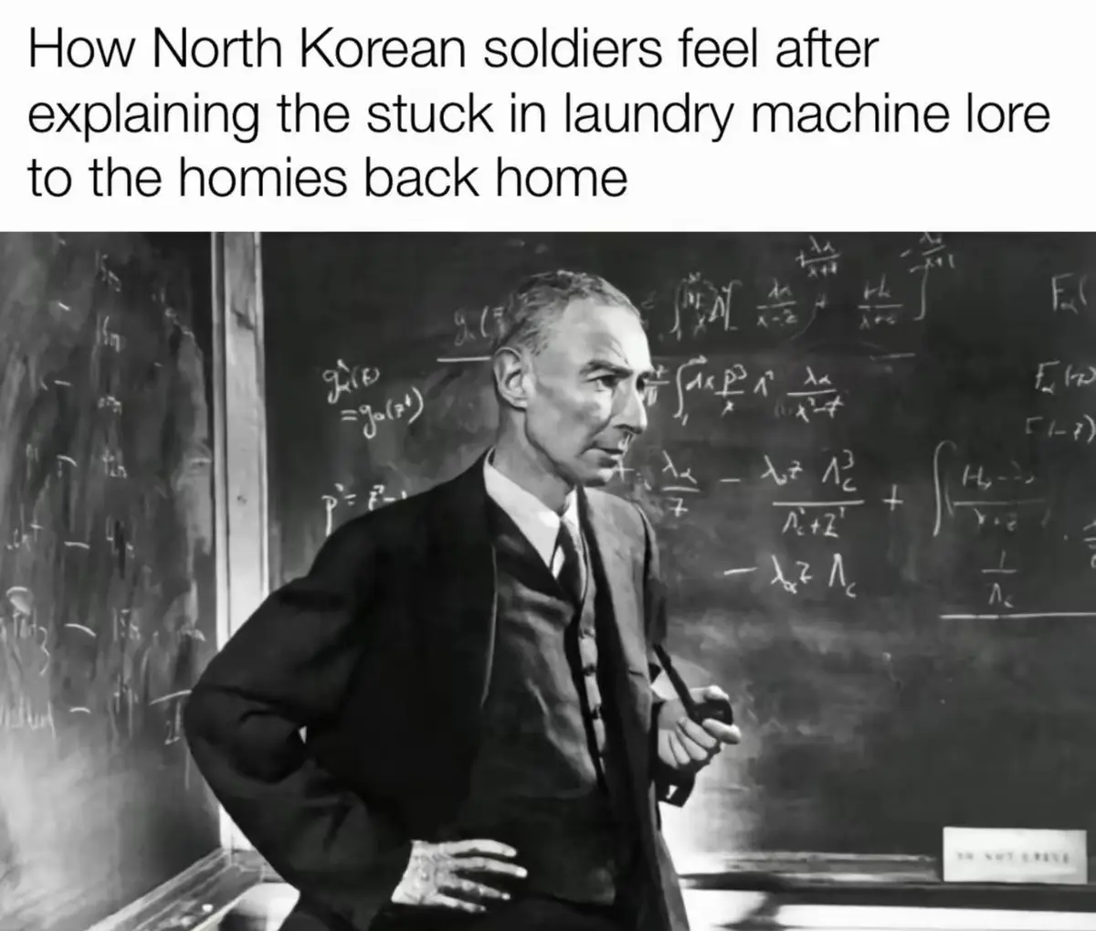 A black-and-white photo shows a man in a suit standing in front of a chalkboard filled with complex mathematical equations…