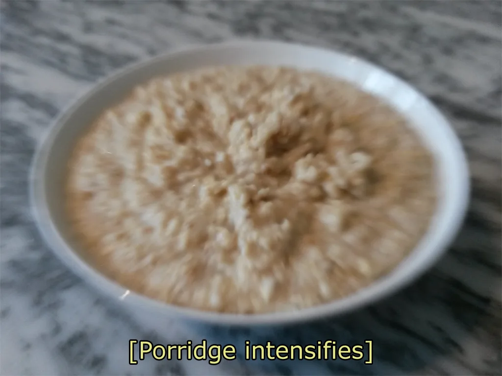 A blurry, out-of-focus photo shows a white bowl filled with oatmeal or porridge resting on a gray and white marbled surface…