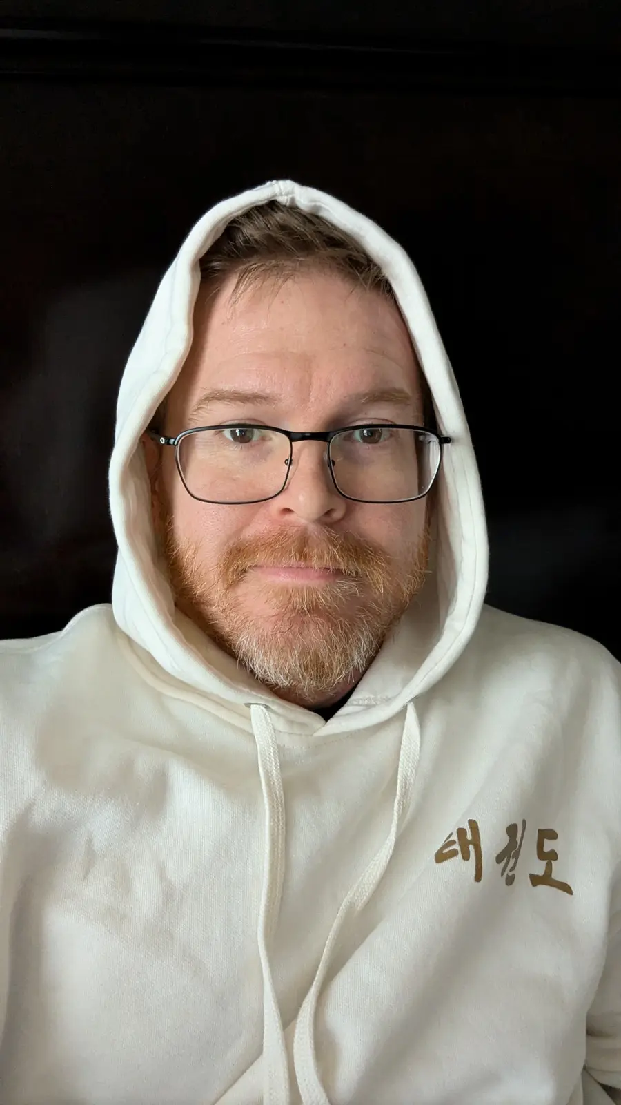 A man with glasses and a red beard wears a white hoodie with the Korean text '대청도' on the left chest. He looks directly at…