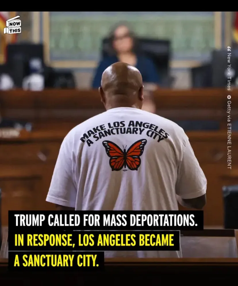 A man is seen from behind in a courtroom, wearing a white t-shirt with the text 'MAKE LOS ANGELES A SANCTUARY CITY' and an…