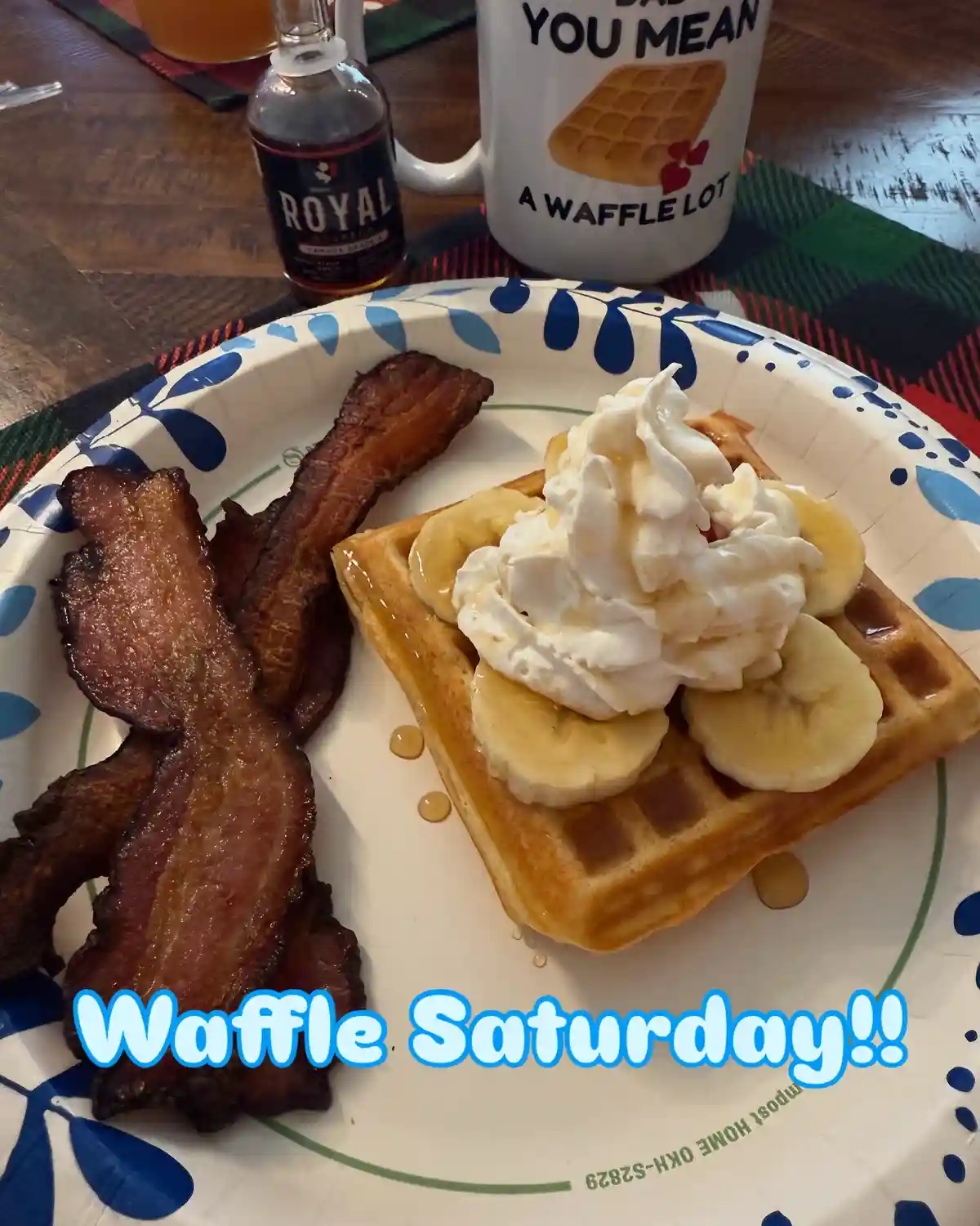 A close-up photo of a breakfast plate with a waffle topped with sliced bananas, whipped cream, and syrup, alongside crispy…