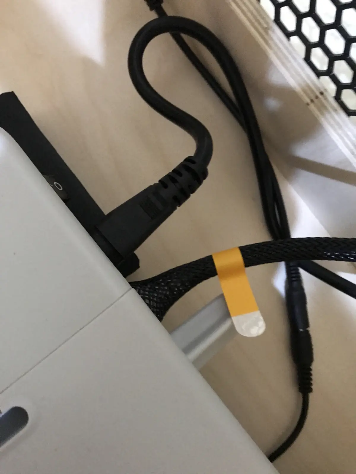 A close-up photo shows a black braided cable with a yellow and white adhesive band-aid taped around it, next to a black…