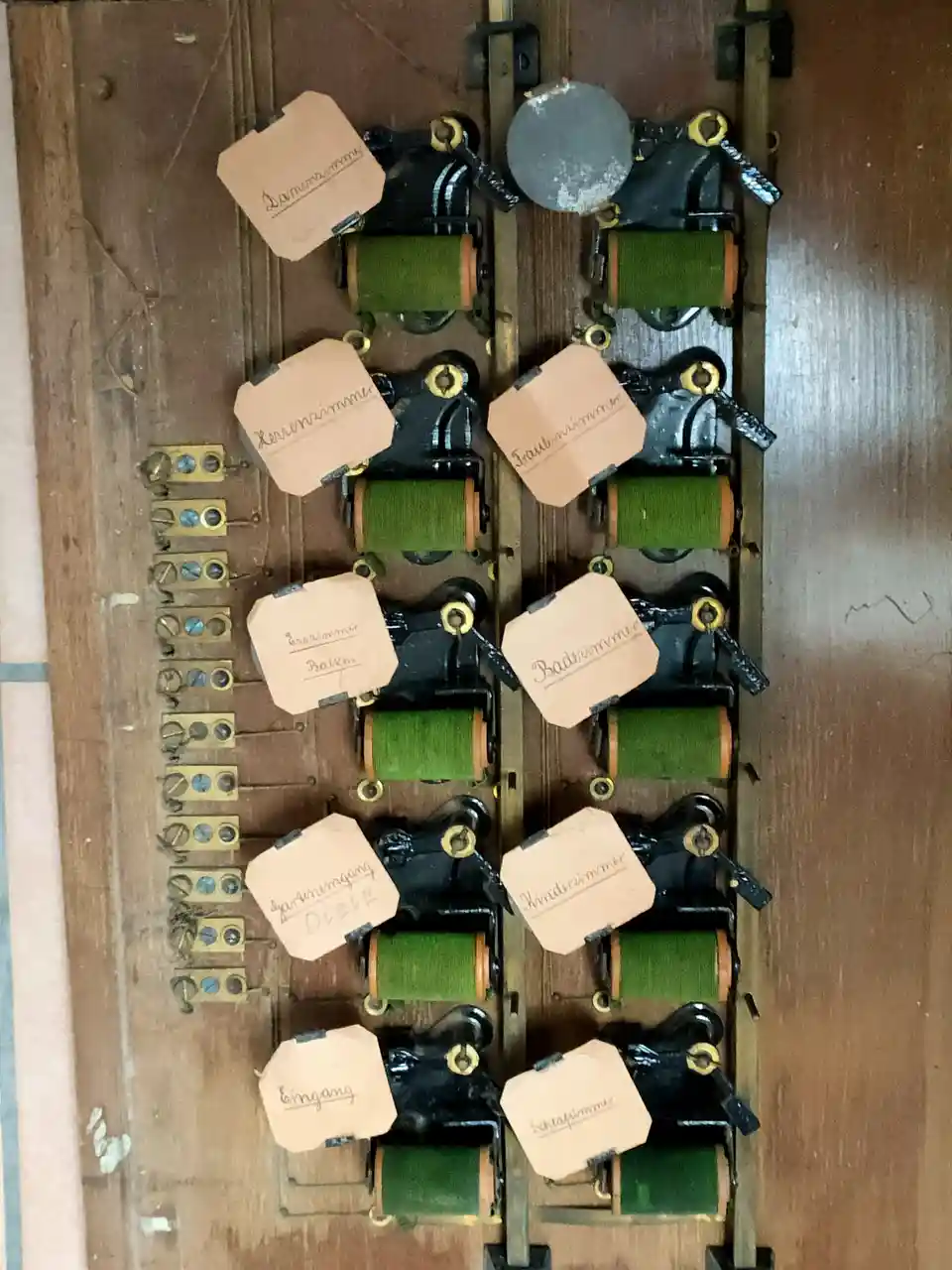 An old-fashioned wooden panel with multiple black mechanical levers, each labeled with handwritten German room names like…