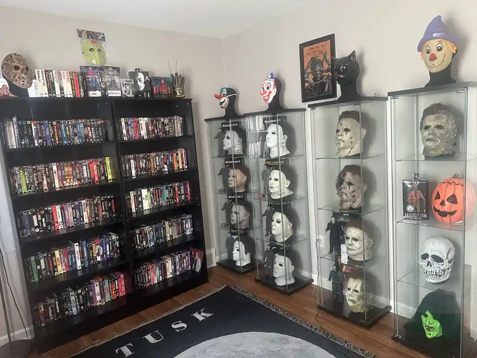 A room filled with horror movie memorabilia, including multiple glass display cases filled with Michael Myers masks from…