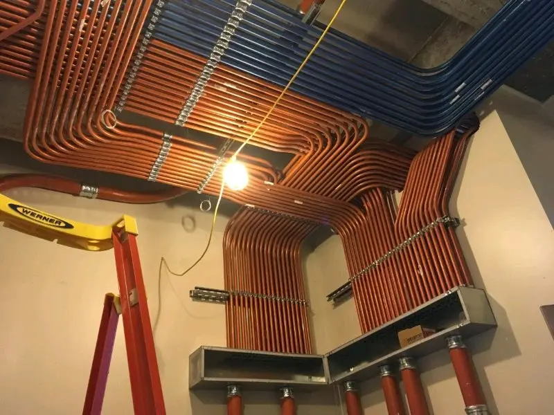 An overhead view of a room with extensive copper and blue pipes running across the ceiling and walls, secured with metal…