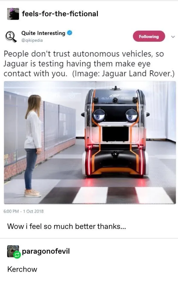 A woman stands facing a futuristic autonomous vehicle with large, glowing blue circular headlights that resemble eyes. The…