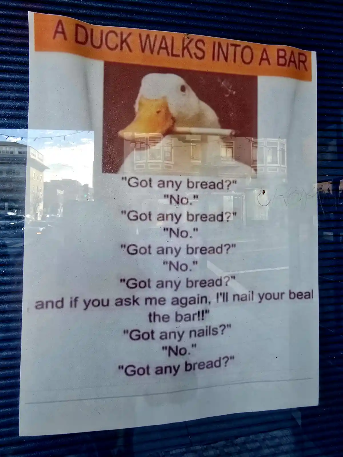 A printed poster taped to a window shows a photo of a duck holding a cigarette, with text telling a joke about a duck…