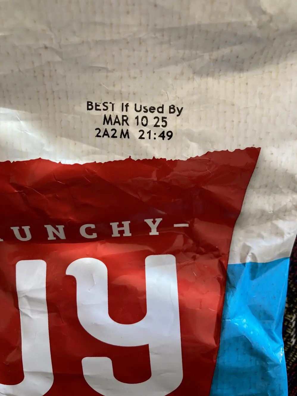 A close-up of a crumpled Lunchy snack bag showing a 'BEST If Used By' date printed as 'MAR 10 25 2A2M 21:49', with the brand…
