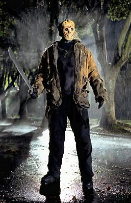 A person in a Jason Voorhees costume stands in a dark, rainy forest holding a machete. The figure wears a hockey mask, a…
