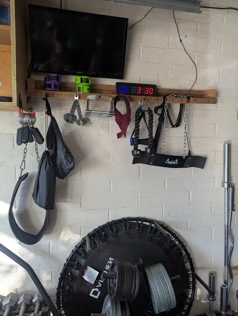 A home gym wall with a digital timer displaying 'H2 3:30' mounted above various fitness equipment including resistance…