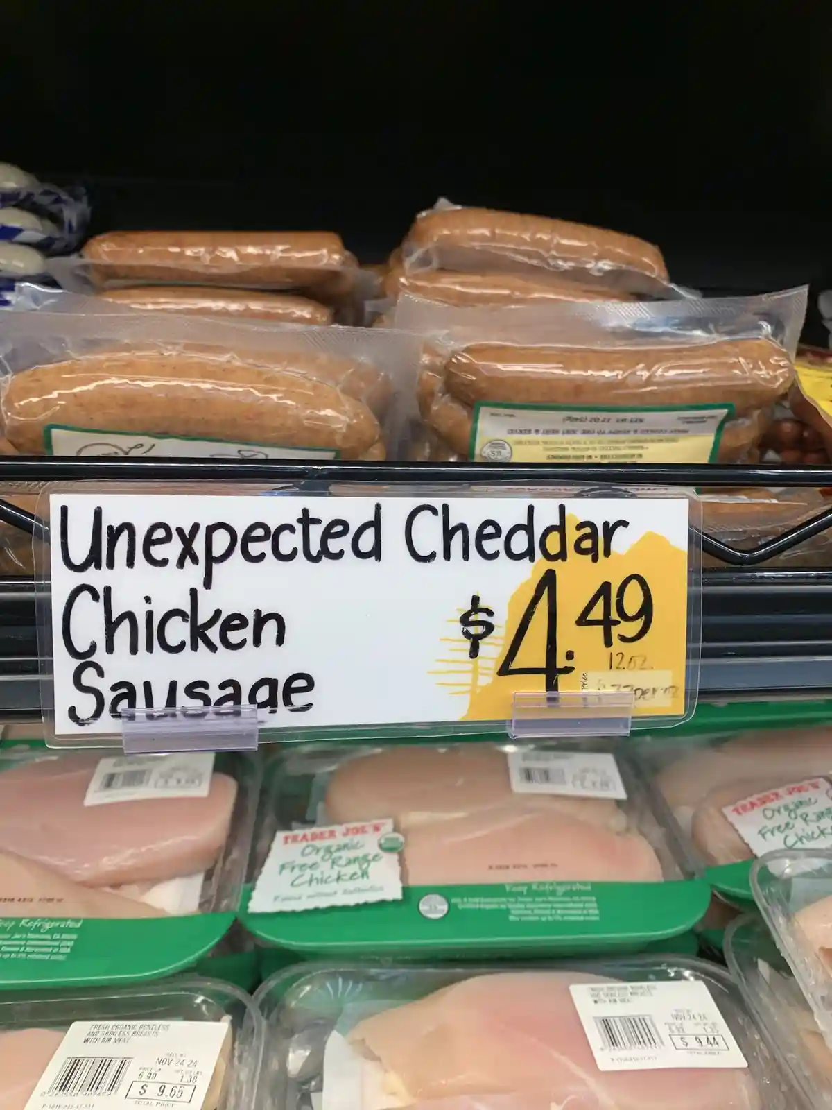 A grocery store meat aisle shelf displays packaged chicken sausages with a handwritten price tag that reads 'Unexpected…