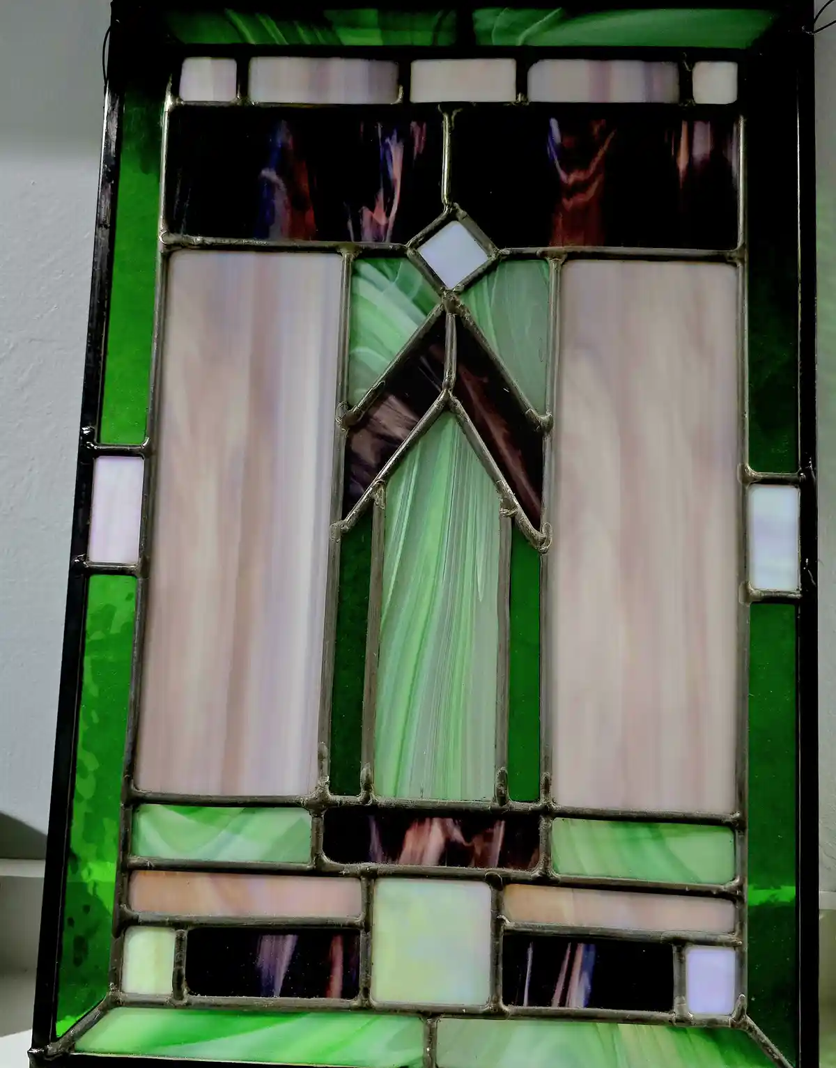 A close-up of a stained glass panel with green, white, and dark purple glass pieces arranged in a geometric pattern, framed…