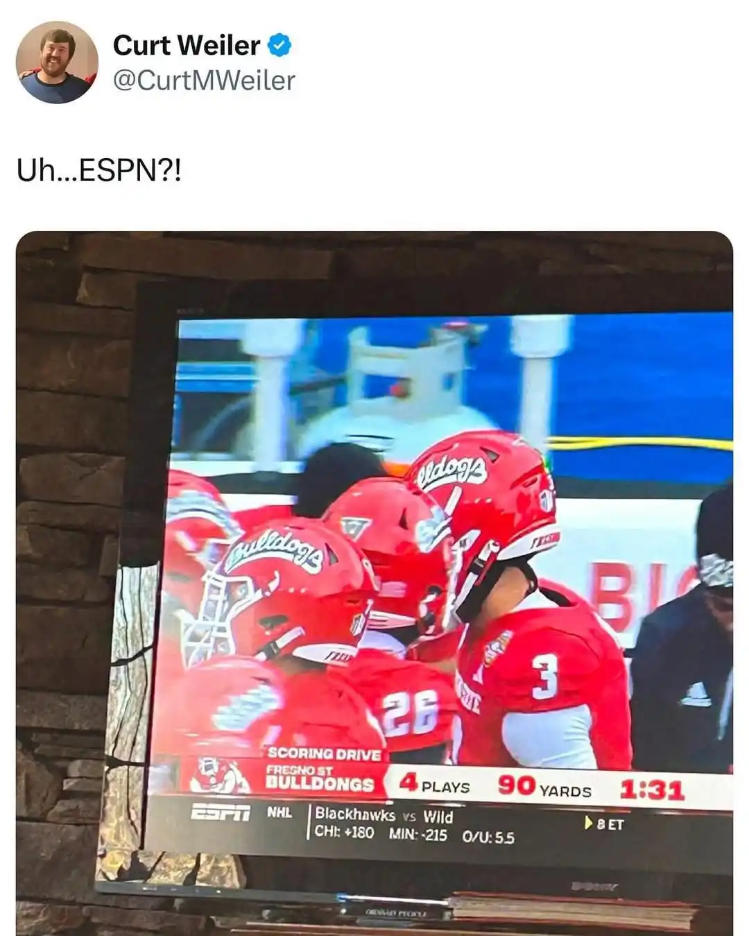 A screenshot of a tweet by Curt Weiler showing a TV screen displaying a football game. The screen shows Fresno St. Bulldogs…