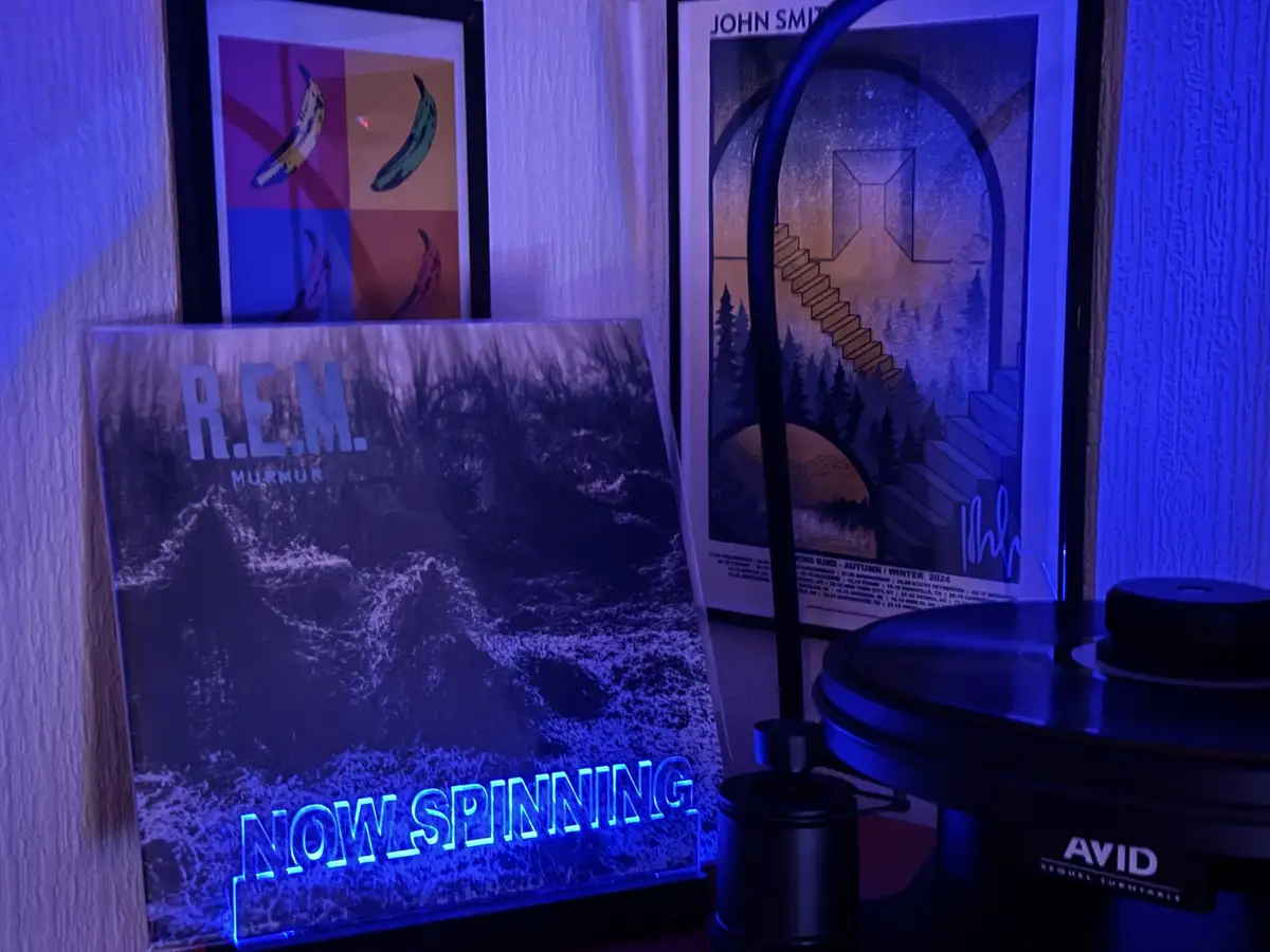 A vinyl record player with an 'AVID' brand turntable is shown next to a standing album cover for R.E.M.'s 'Murmur'. The…