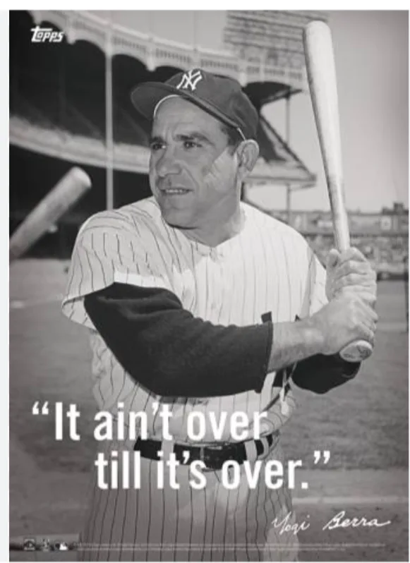 A black-and-white vintage baseball photo shows Yogi Berra in a New York Yankees pinstripe uniform holding a bat, looking…