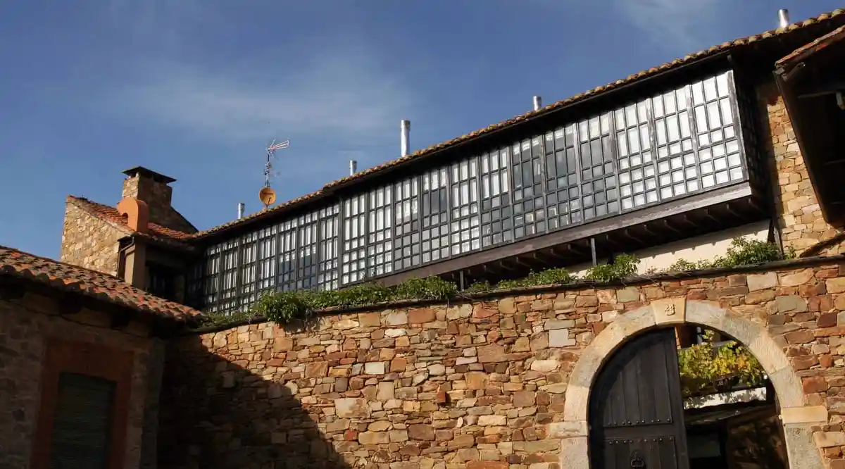 A low-angle photo shows a rustic stone building with a long, modern-looking black-framed window structure on its upper…