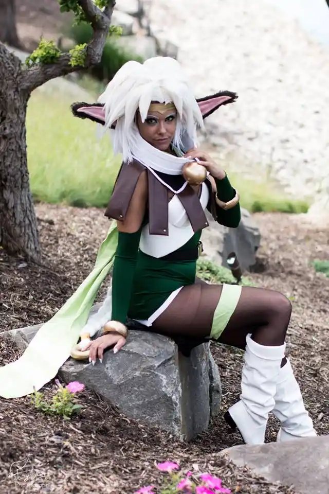 A person in a detailed cosplay of a white-haired, pointed-eared anime character sits on a rock outdoors, holding a small…