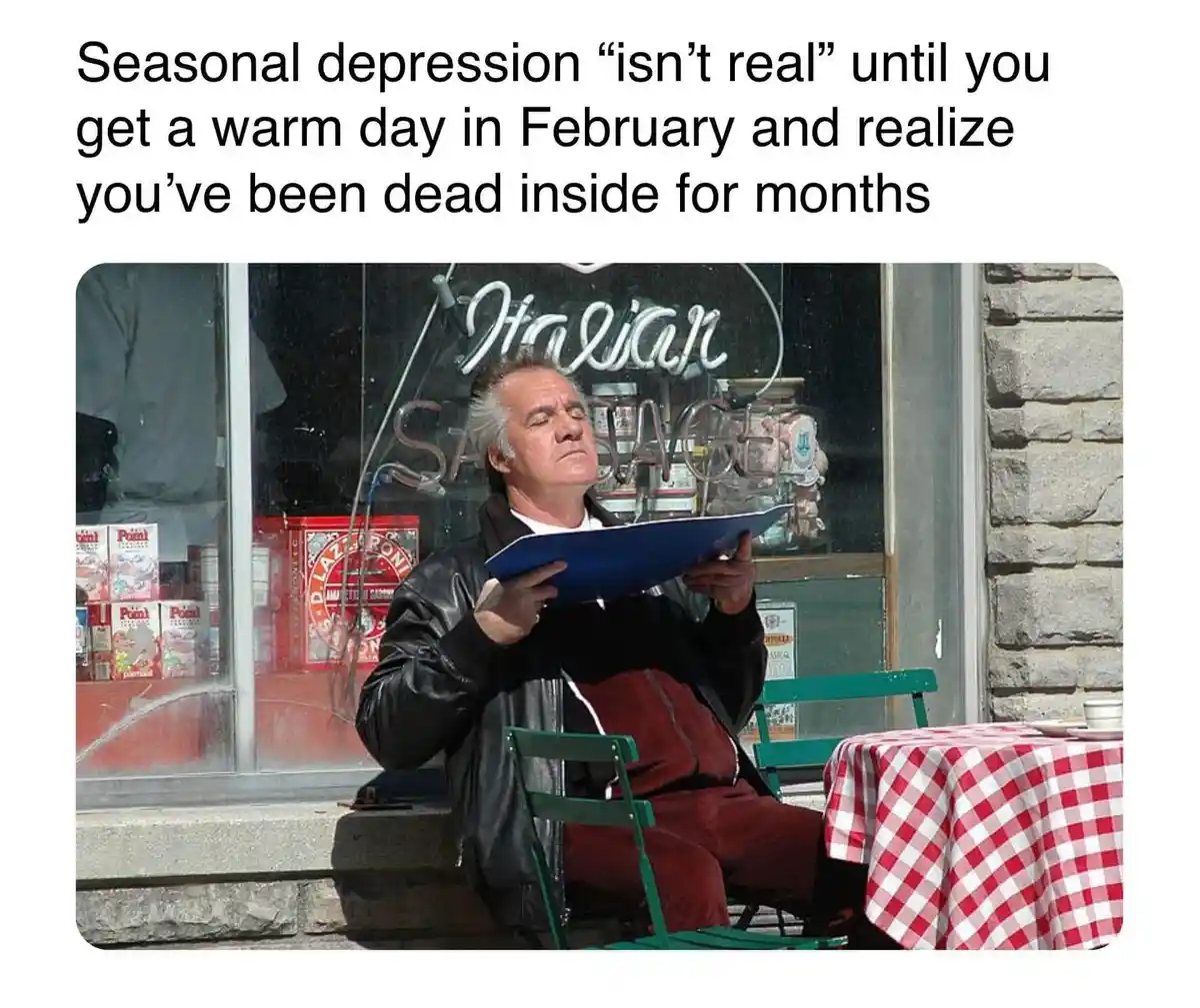 A man sits outside an Italian restaurant, looking exhausted and disinterested while holding a blue folder. Behind him, a…