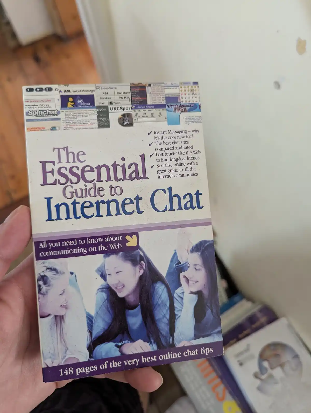 A hand holds a physical book titled 'The Essential Guide to Internet Chat' from the early 2000s, featuring a cover with…